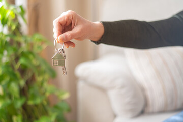 Real estate agent holding house keys with a house-shaped keychain in a cozy living room, featuring a green plant and a sofa, symbolizes new home ownership and property investment