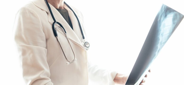 Doctor wearing a stethoscope examines a spine x-ray, assessing bone density and looking for signs of osteoporosis, paget's disease, or osteomyelitis