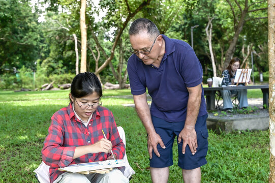 Senior art teacher teaching artist girl to paint in outdoor art class