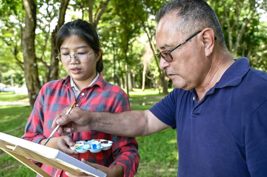 Senior art teacher teaching artist girl to paint in outdoor art class