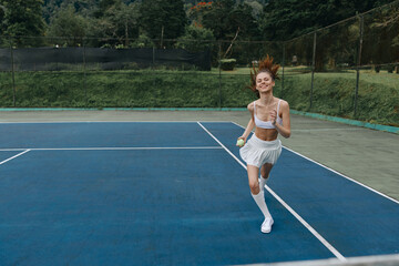 Fototapeta premium Young woman playing tennis, smiling with joy on a sunny day, wearing a sporty outfit in white, on a vibrant green court with a clear blue sky background