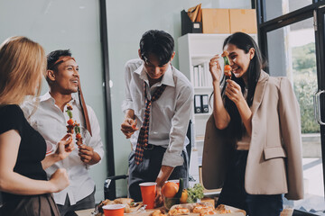 Asian office colleagues and friends enjoy a daytime BBQ with pizza and beer, celebrating Halloween and cheering for their favorite soccer team, creating a lively atmosphere filled with joy.