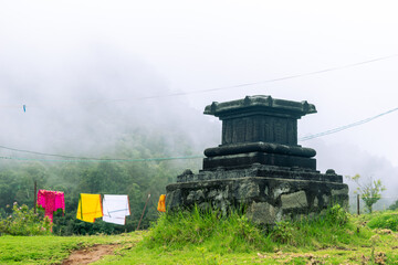 Obraz premium Ancient stone architecture stands in Kodaikanal, surrounded by lush greenery and colorful textiles hanging to dry in the cool mist.