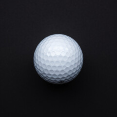 A photo of a white golf ball against a completely black background. The golf ball has a smooth and glossy surface. The deep black background provides a stark contrast.