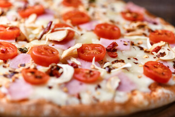 Pizza with ham, cherry tomatoes and mozzarella cheese. Wooden background. Soft focus. Close up.