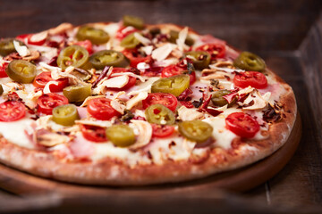 Pizza with ham, cherry tomatoes and mozzarella cheese. Wooden background. Soft focus. Close up.