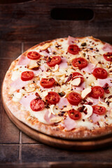 Pizza with ham, cherry tomatoes and mozzarella cheese. Wooden background. Soft focus. Close up.