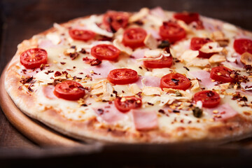 Pizza with ham, cherry tomatoes and mozzarella cheese. Wooden background. Soft focus. Close up.