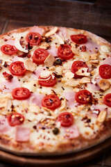 Pizza with ham, cherry tomatoes and mozzarella cheese. Wooden background. Soft focus. Close up.