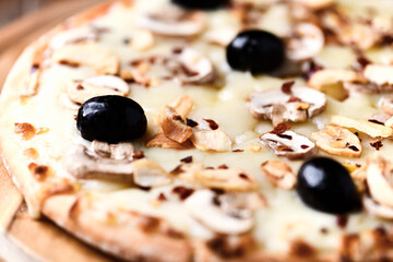 Pizza with champignons, black olives and mozzarella cheese. Wooden background. Soft focus.