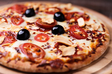 Pizza with salami and mozzarella cheese, jalapeno pepper and black olives. Wooden background. Soft focus. Close up.	