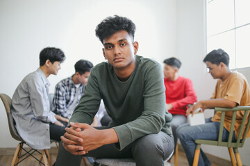 Fototapeta premium Portrait Of Young Indian Man Posing Against Group Therapy Session Sitting in Circle Background