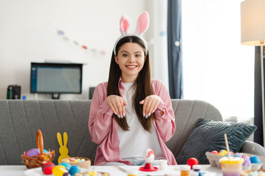 Smiling, attractive teen girl showing painted nails while decorating easter eggs at home