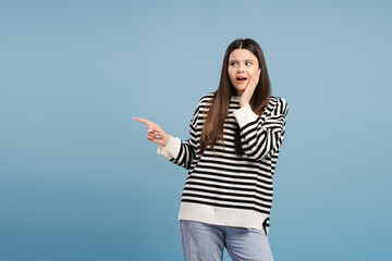 Surprised young girl pointing finger showing something exciting on blue background