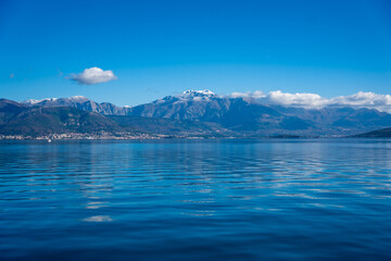 Bay of Kotor in Montenegro and the top of high snow-capped mountains, small settlements on the coast and the bright blue waters of the Adriatic Sea.