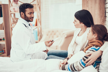 Indian doctor seeing patients at home. Doctor is taking temperature of girl with pregnant mother.