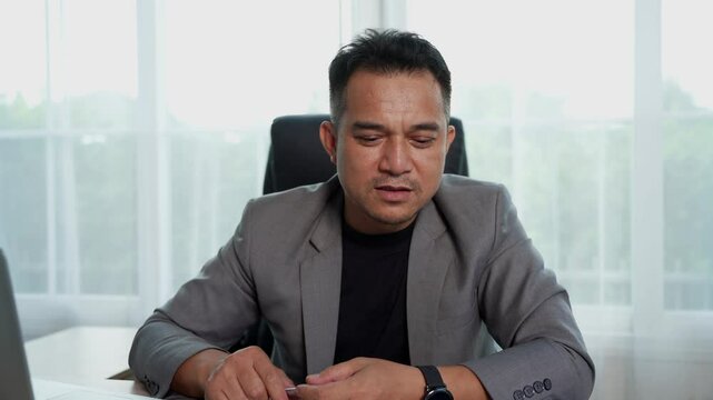 Medium shot, Front view, Asian middle-aged businessman in formal suit at modern office setting. He talking with seriously during video all.