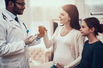 Fototapeta premium Indian doctor seeing patients in office. Doctor is giving mixture to pregnant woman with daughter.