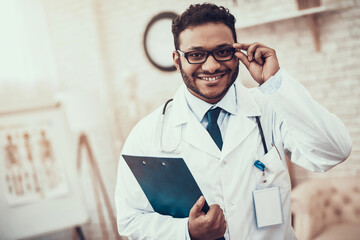 Indian doctor seeing patients in office. Doctor is posing in glasses with clipboard.