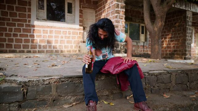 Bearded man sits drinking liquor lost in thought outside