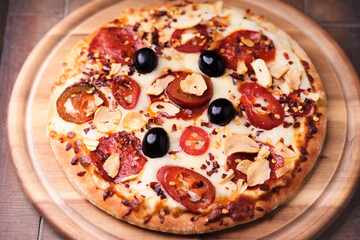 Pizza with salami and mozzarella cheese, jalapeno pepper and black olives. Wooden background. Soft focus. Close up.	