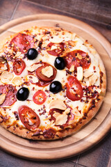 Pizza with salami and mozzarella cheese, jalapeno pepper and black olives. Wooden background. Soft focus. Close up.	