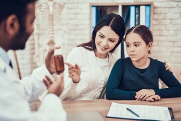 Indian doctor seeing patients in office. Doctor is giving mother and daughter cough syrup.