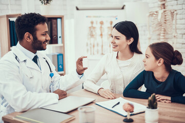 Indian doctor seeing patients in office. Doctor is giving mother and daughter bottle of pills.