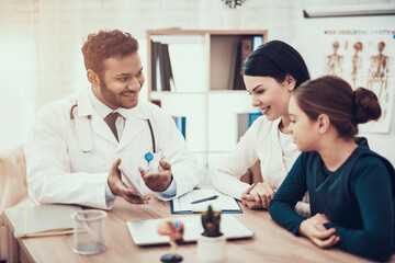Obraz premium Indian doctor seeing patients in office. Doctor is showing tablet to mother and daughter.