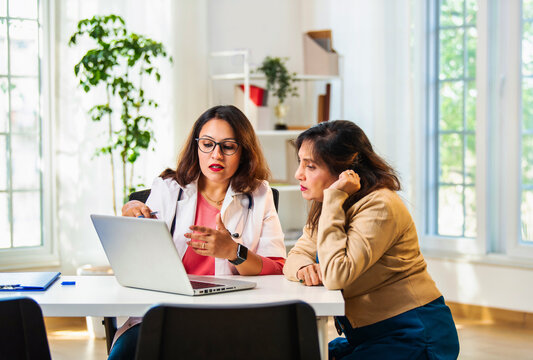 Indian Young doctor consulting senior patient with a laptop, explaining diagnosis in a luxury clinic