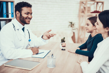 Fototapeta premium Indian doctor seeing patients in office. Mother and daughter are listening to doctor.