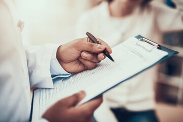 Indian doctor seeing patients in office. Doctor is taking notes on woman's symptoms.
