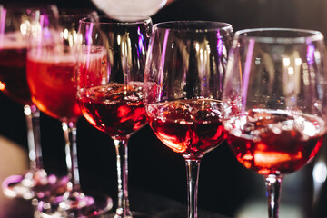 Bartender working, barman mixing and pouring drinks and beverages in a club, beautiful row line of different red coloured liquor alcohol cocktails on a party in a bar, catering banquet on event