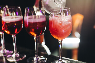 Bartender working, barman mixing and pouring drinks and beverages in a club, beautiful row line of different red coloured liquor alcohol cocktails on a party in a bar, catering banquet on event