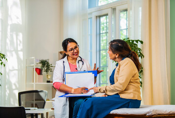 Indian Young female doctor discussing medical case report with senior patient in a lavish clinic