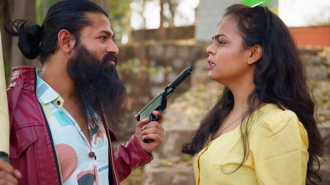 Bearded man with a gun threatens the woman outdoors