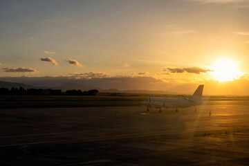 A propeller passenger plane stands on an empty airport tarmac as the sun sets.