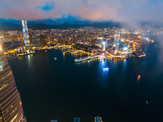 Obraz premium Aerial panorama of Hong Kong city at night, showcasing the skyline, water, and lights under a cloudy sky.