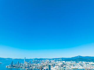Obraz premium Aerial panorama of Hong Kong city with skyscrapers and mountains under a clear blue sky, showcasing a stunning cityscape view.