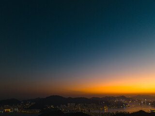 Aerial panorama captures Hong Kong city at twilight.  Glowing city lights punctuate the dark landscape against a gradient sky from blue to orange.