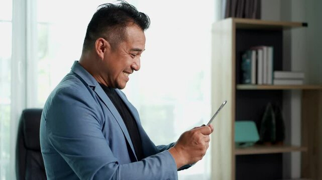 Professional businessman smiling while uses tablet in modern office. he appears engaged and happy, possibly receiving good news, as indicated by his facial expression and body language