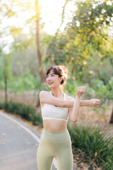 Asian woman stretching before workout outdoors in park, enjoying fresh air and sunlight. She wears activewear, preparing for healthy exercise routine. sport and healthy lifestyle concept