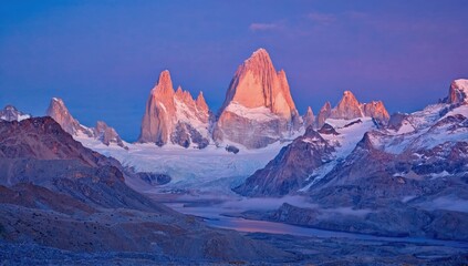 Colorful sunrise illuminates the jagged peaks of Torres del Paine National Park in Chile. Snow-capped mountains tower over valleys and glacial lakes, creating a stunning vista