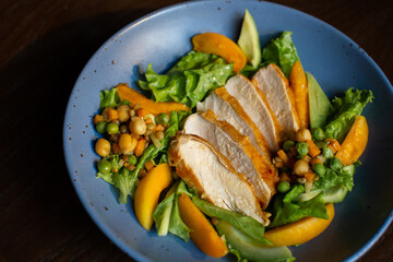 juicy fried chicken with vegetables and sweet peaches on a blue plate