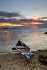 Traditional sailing and rowing fisherman boat. Dramatic gold sunset sky background