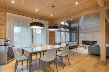A cozy room with a dining table and chairs in the interior of a wooden mansion. Wide .passage to...