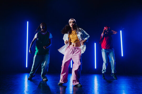Group of hip hop dancer dancing together in a moody studio with tube neon lights.