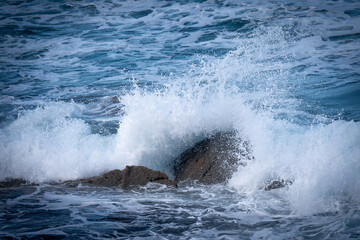 Fototapeta premium A powerful ocean wave crashing against coastal rocks, sending white spray into the air