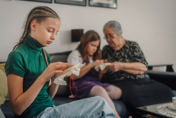 Obraz premium Girls learning cross-stitch embroidery with grandmother at home