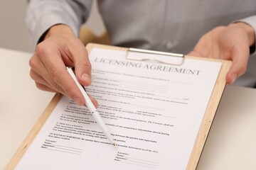 Man with pen pointing at licensing agreement document at white table indoors, closeup
